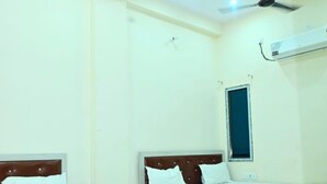 A hotel room with two beds, a ceiling fan, an air conditioning unit, and a window. - Hotel Narayan Palace (Danta Ramgarh)