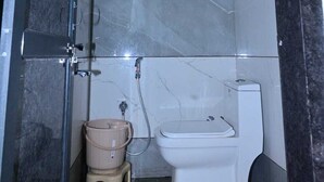 A bathroom with a shower, toilet, and a small stool. - Hotel Narayan Palace (Danta Ramgarh)