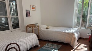 Une chambre avec deux lits, une chaise, une petite table et une fenêtre donnant sur un paysage verdoyant.