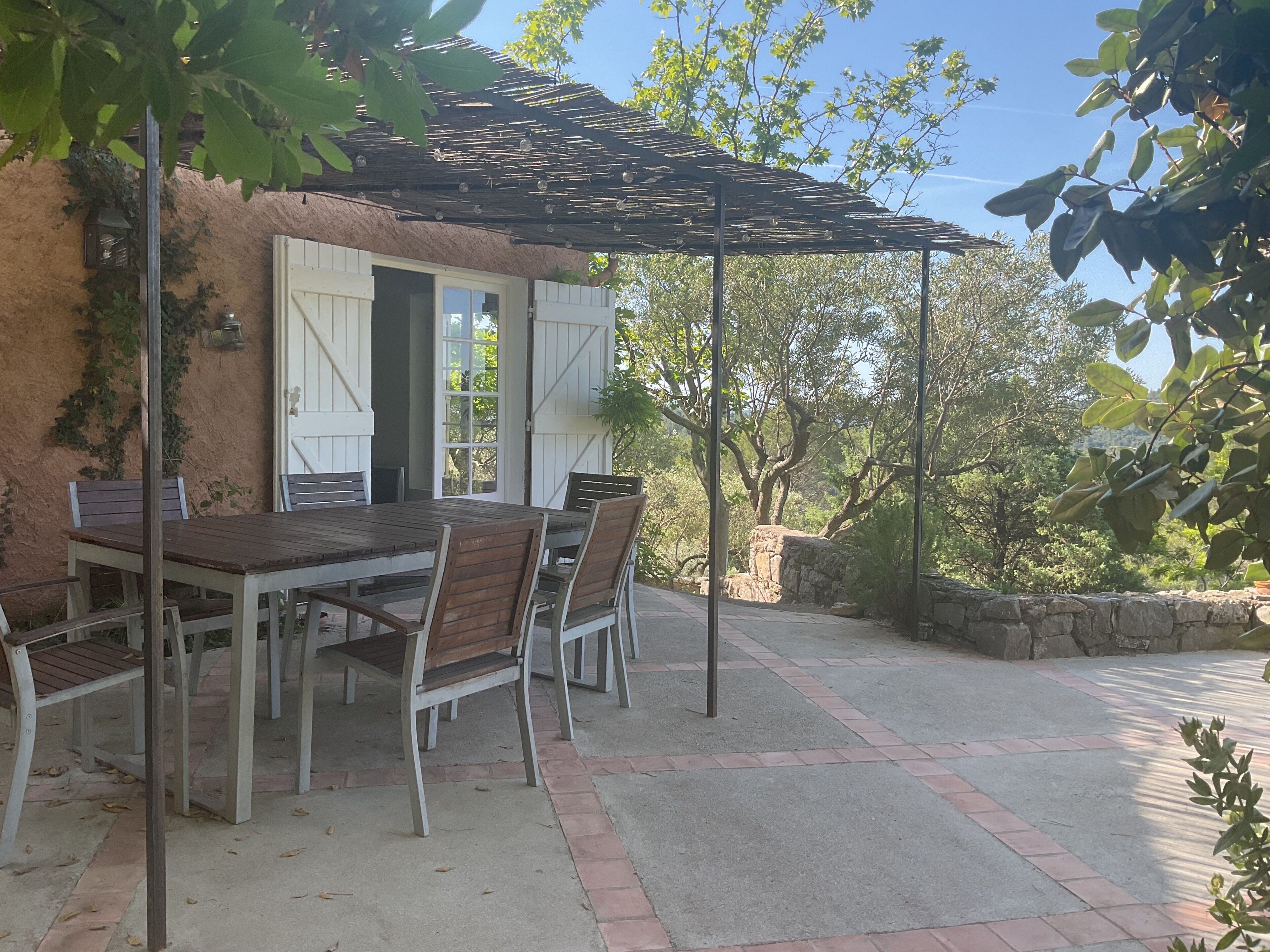An outdoor patio with a table and chairs, a pergola, and a stone wall.