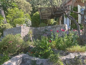 A stone wall with a wooden pergola and a variety of flowering plants.