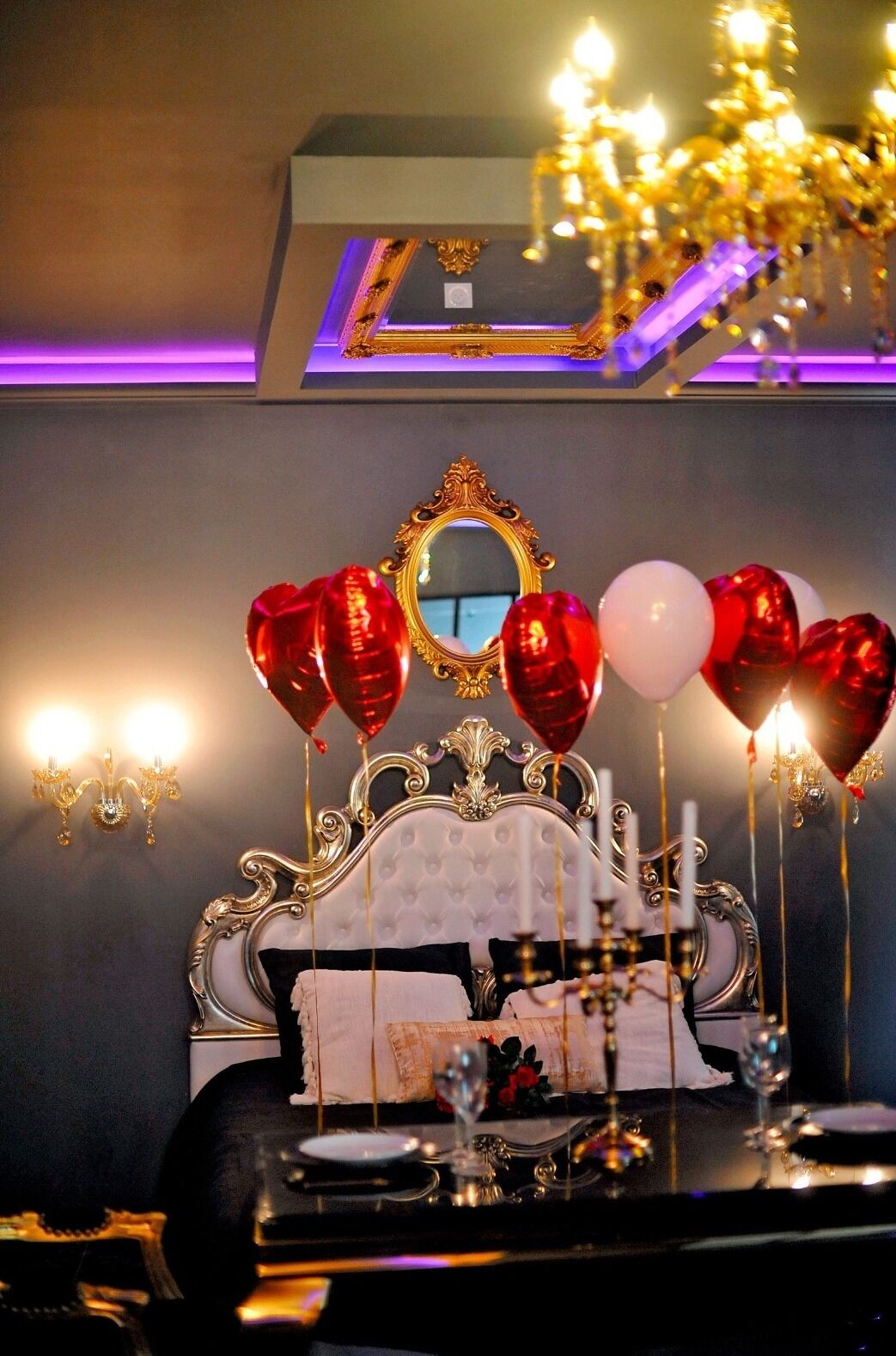 A bed with a decorative headboard, a mirror, and a bedside table with candles and a glass.