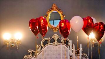 A bed with a decorative headboard, a mirror, and a bedside table with candles and a glass.
