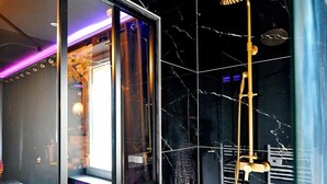 Une salle de bain moderne avec des carreaux de marbre noir, une douche en verre et un meuble-lavabo apparent.