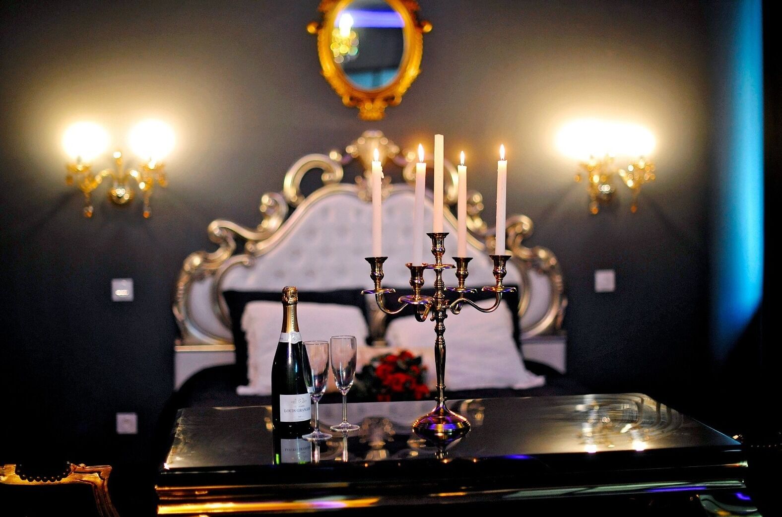 Een luxueuze slaapkamer met een bed, nachtlampen, een kandelaar en champagneflessen.