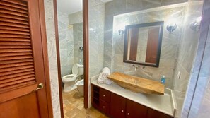 A bathroom with a marble wall, a wooden vanity, a mirror, and a toilet.