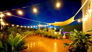 Un espace extérieur aménagé en terrasse, agrémenté de guirlandes lumineuses, de plantes en pot et d’un auvent jaune.