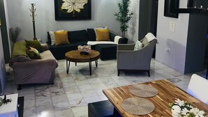 Un salon moderne doté d’un ventilateur de plafond, d’une grande œuvre d’art représentant des feuilles, d’un canapé, d’une table basse et d’une table à manger avec des sets de table.