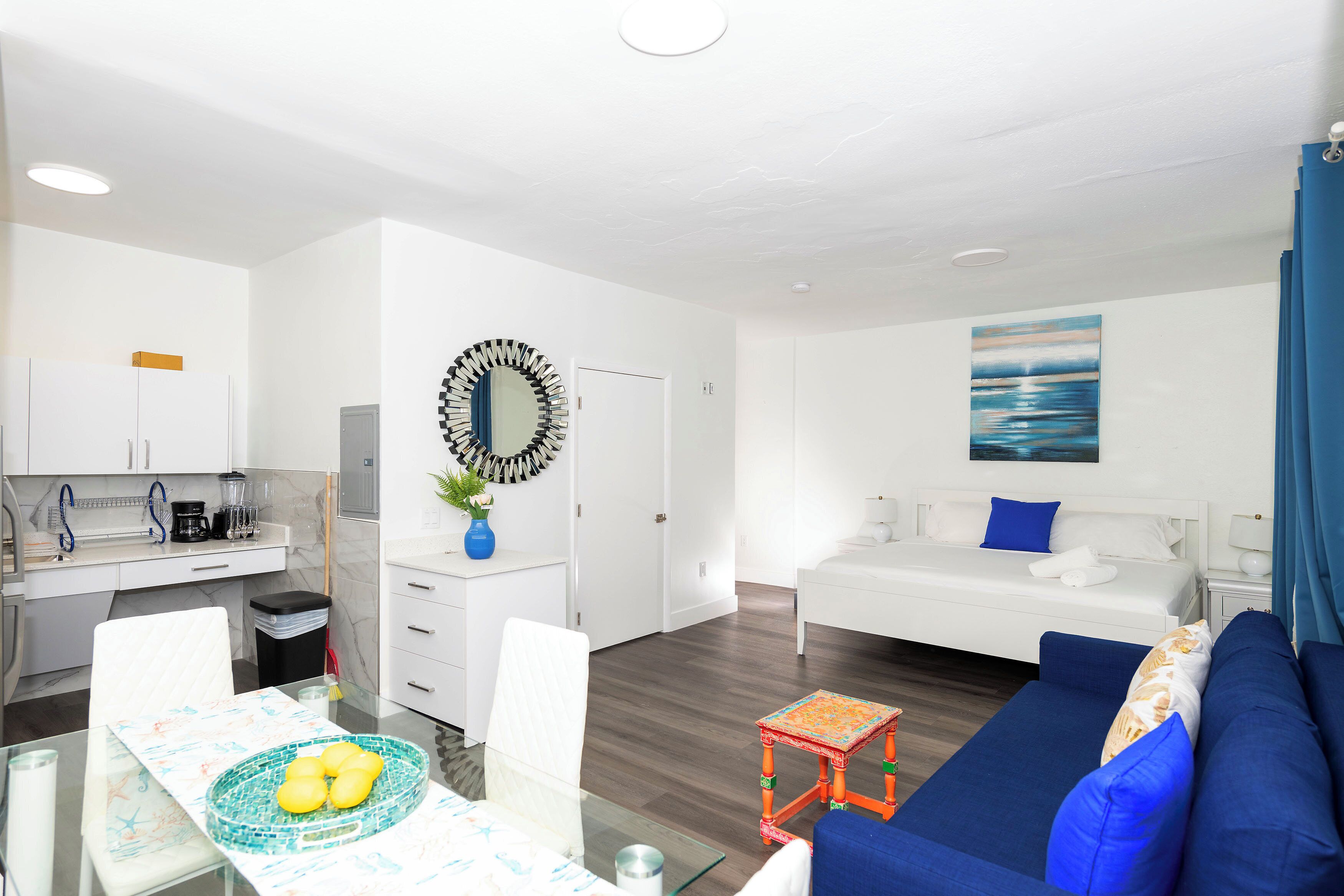 A modern, well-lit room with a dining table, a sofa, a bed, and a kitchen area.