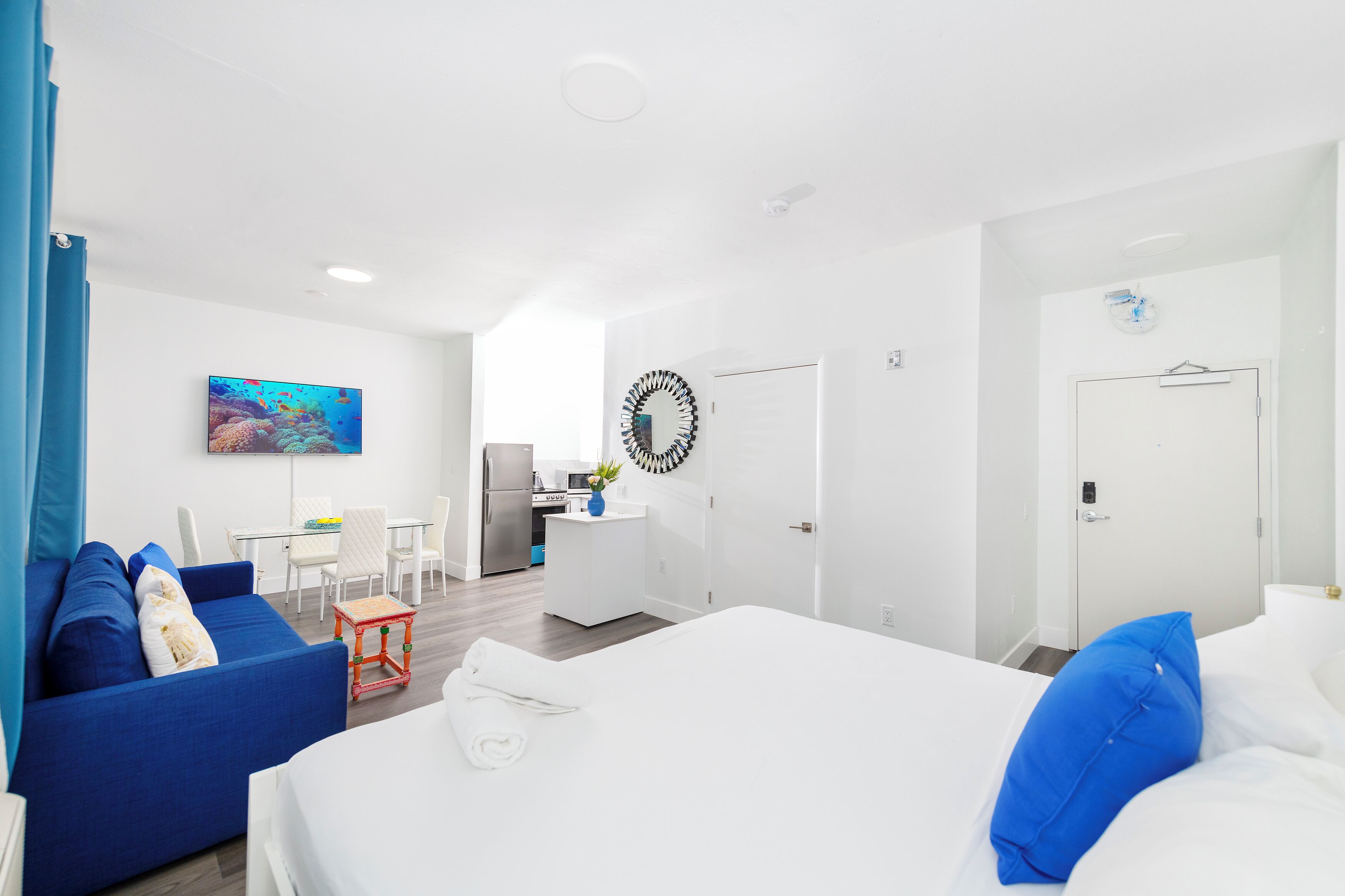 Ein modernes Hotelzimmer mit einem Bett, einem blauen Sofa, einem kleinen Esstisch und einer Küchenzeile.