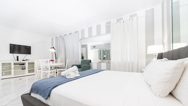 A modern hotel room with a large bed, a desk with a chair, a TV, and a mirror. - Collins Beach Apartments (Miami Beach)
