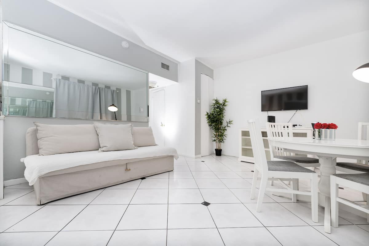 A modern living room with a sofa, dining table, chairs, a TV, and a potted plant.