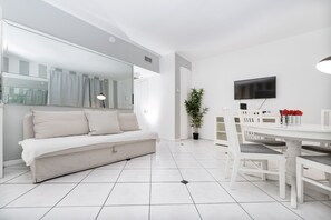 A modern living room with a sofa, dining table, chairs, a TV, and a potted plant.