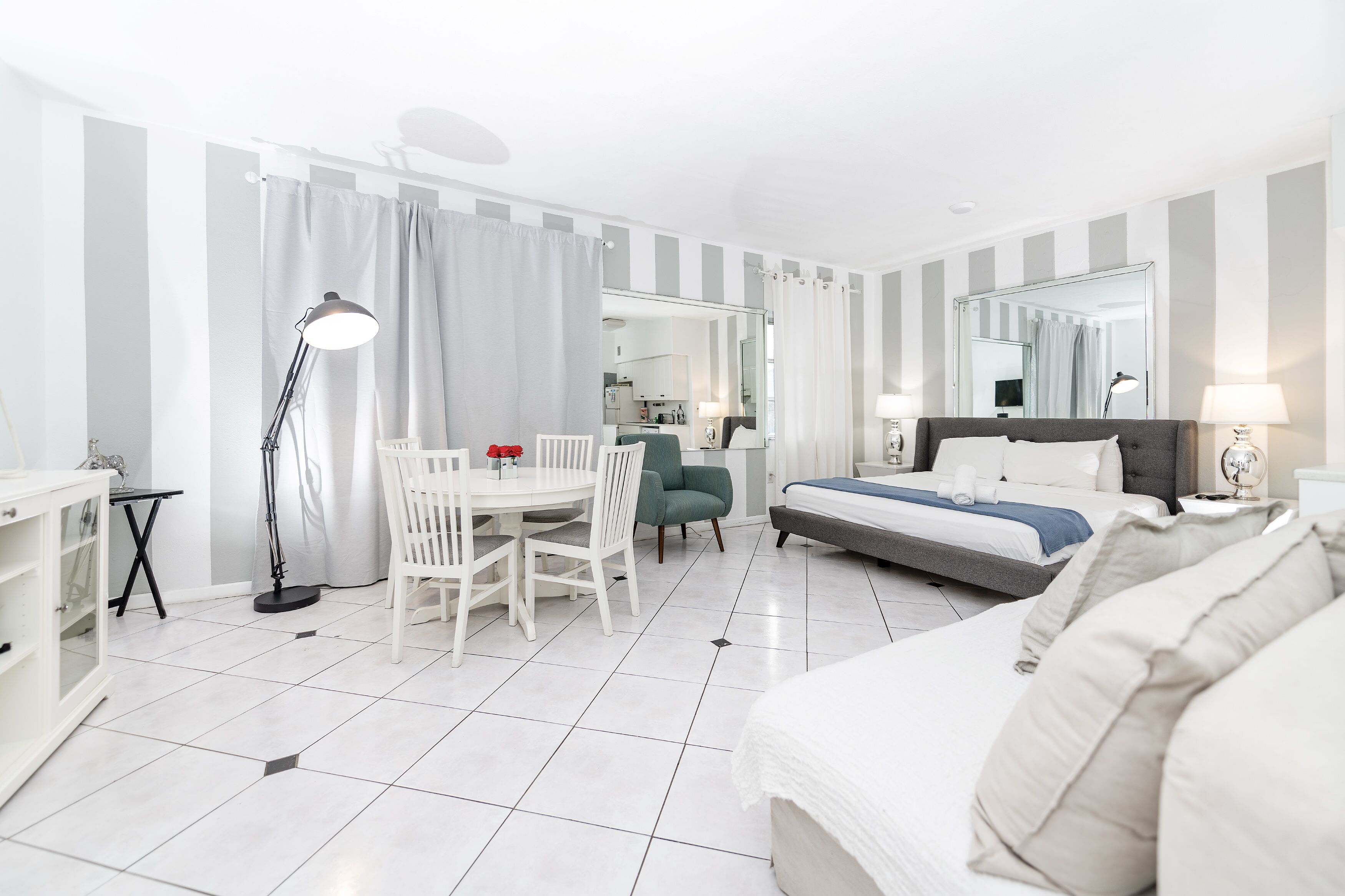 A hotel room with a bed, a desk, a chair, a lamp, and a mirror.
