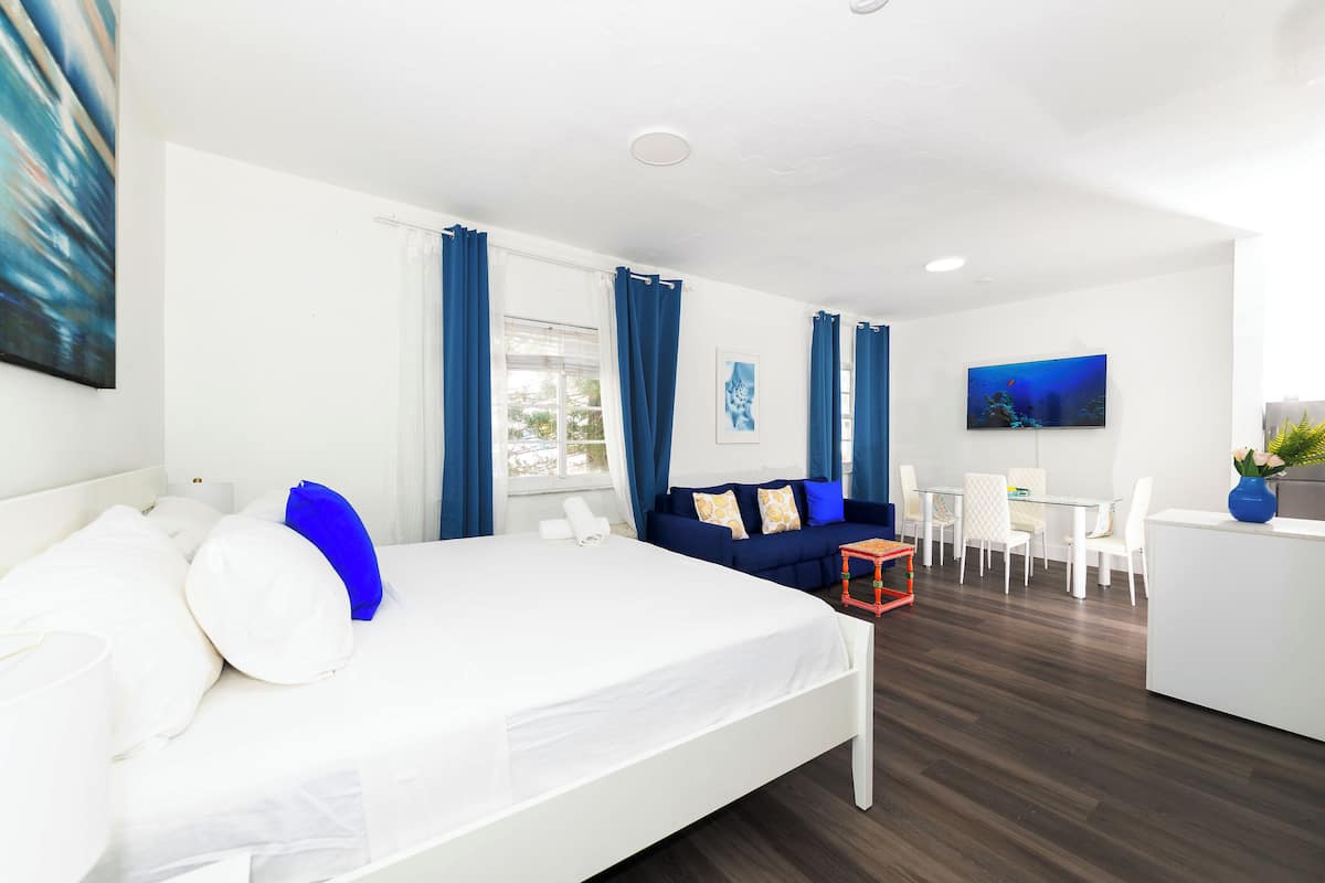 A modern hotel room with a large bed, a sofa, a dining area, and a TV.