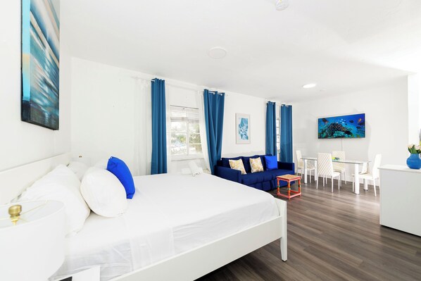 A modern hotel room with a large bed, a sofa, a dining area, and a TV.