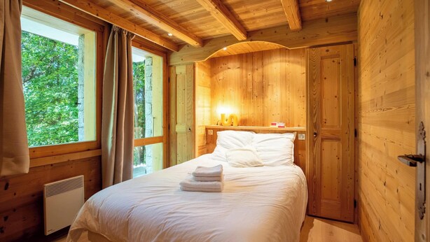 Een slaapkamer in een houten hut met een bed, een raam en een deur.