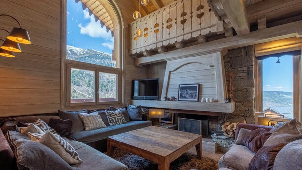 A cozy living room with a fireplace, wooden beams, and large windows offering a mountain view. - Chalet Altaïr with sauna, hot tub and hamam (Les Allues)