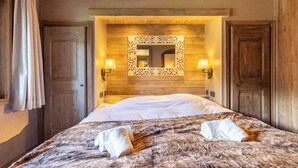 A bedroom with a wooden headboard, a large mirror, two wall-mounted lamps, and a fluffy bedspread. - Chalet Altaïr with sauna, hot tub and hamam (Les Allues)