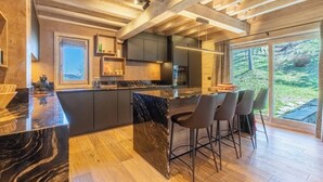 A modern kitchen with a marble island, bar stools, and a large window overlooking a garden. - Chalet Altaïr with sauna, hot tub and hamam (Les Allues)