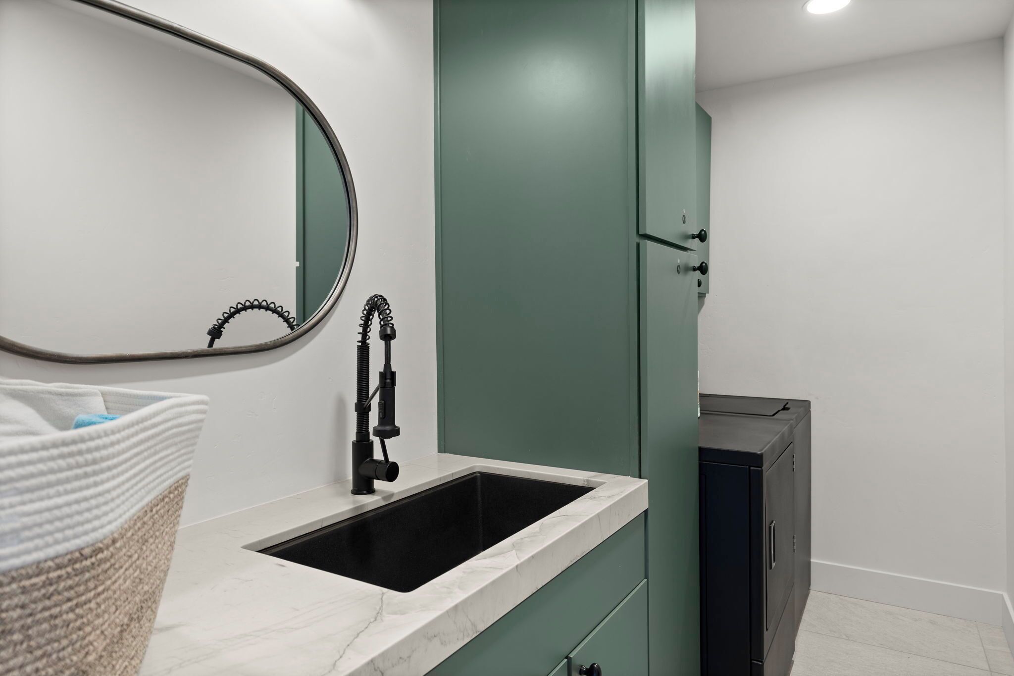 Baño con lavamanos blanco, grifo negro, mueble verde y espejo.