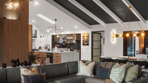 Un salon moderne avec un canapé en cuir foncé, un mur d’accent en bois et une cuisine en arrière-plan.