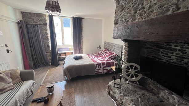 Une chambre confortable avec une cheminée en pierre, un lit avec une literie à motifs, une table basse en bois et un luminaire suspendu.