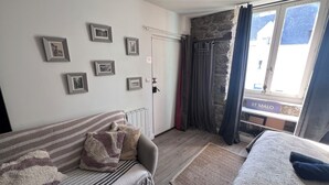 Une pièce confortable avec un canapé, un lit, un radiateur, un mur en pierre et une fenêtre avec des rideaux.