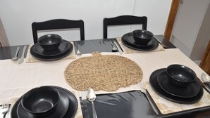 Una mesa de comedor dispuesta con platos, tazones y cubiertos negros, rodeada de sillas negras.