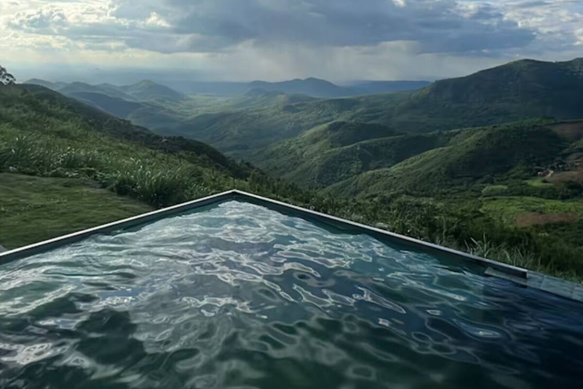 Une piscine à débordement offrant une vue sur des collines verdoyantes et un ciel nuageux.