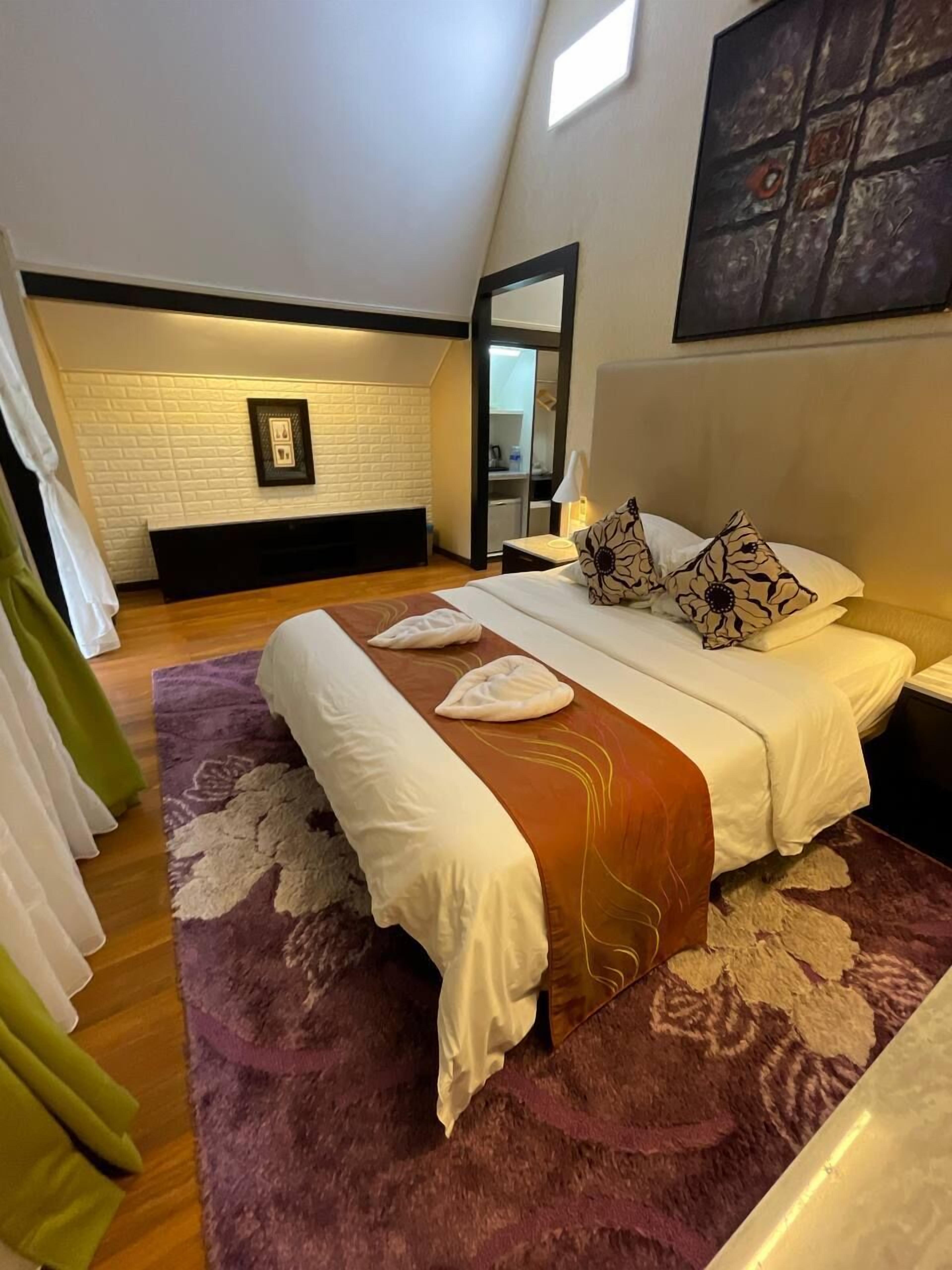 Een slaapkamer met een groot bed, een paars vloerkleed en een witte bakstenen muur.