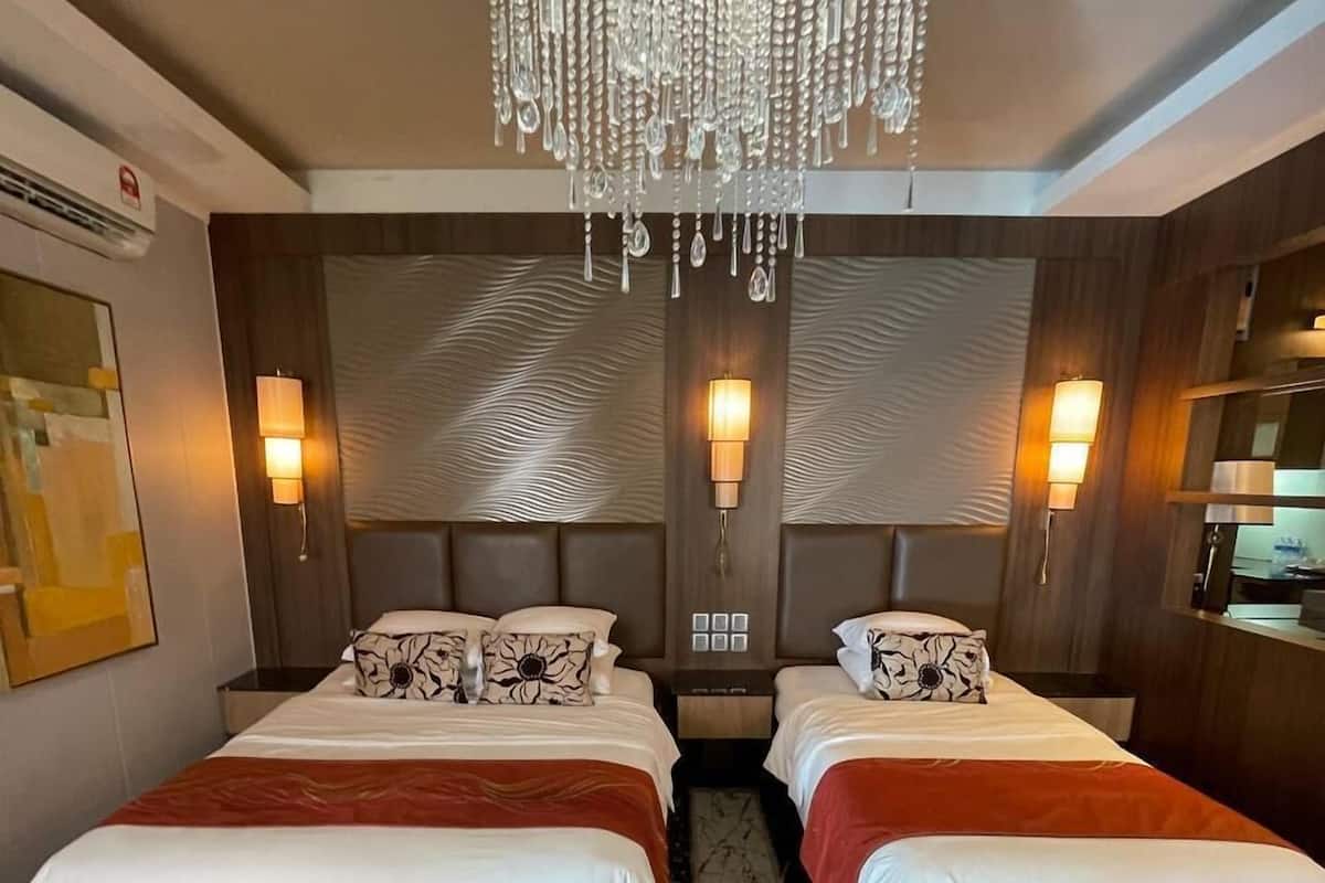 Ein Hotelzimmer mit zwei Betten, einer Kandelaber, Wandleuchten und einem gemusterten Teppich.