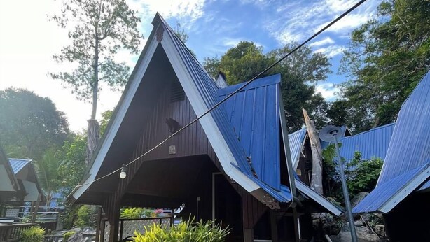 A traditional wooden structure with a sloped roof, surrounded by lush greenery and a clear sky. - CoralView Perhentian Besar Resort (Pulau Perhentian Besar)