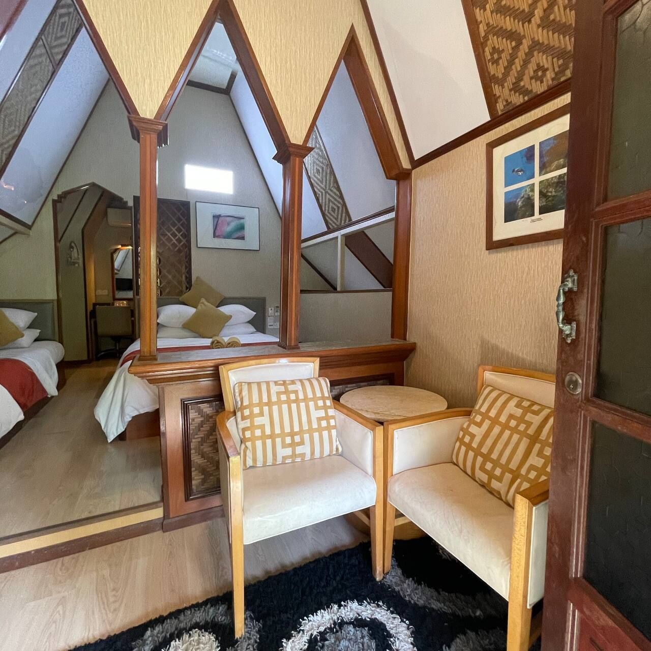 A cozy room with a bed, a desk, and a chair, featuring a unique triangular ceiling design.