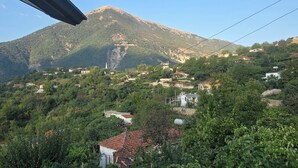 A mountainous landscape with scattered buildings, dense greenery, and a clear sky.