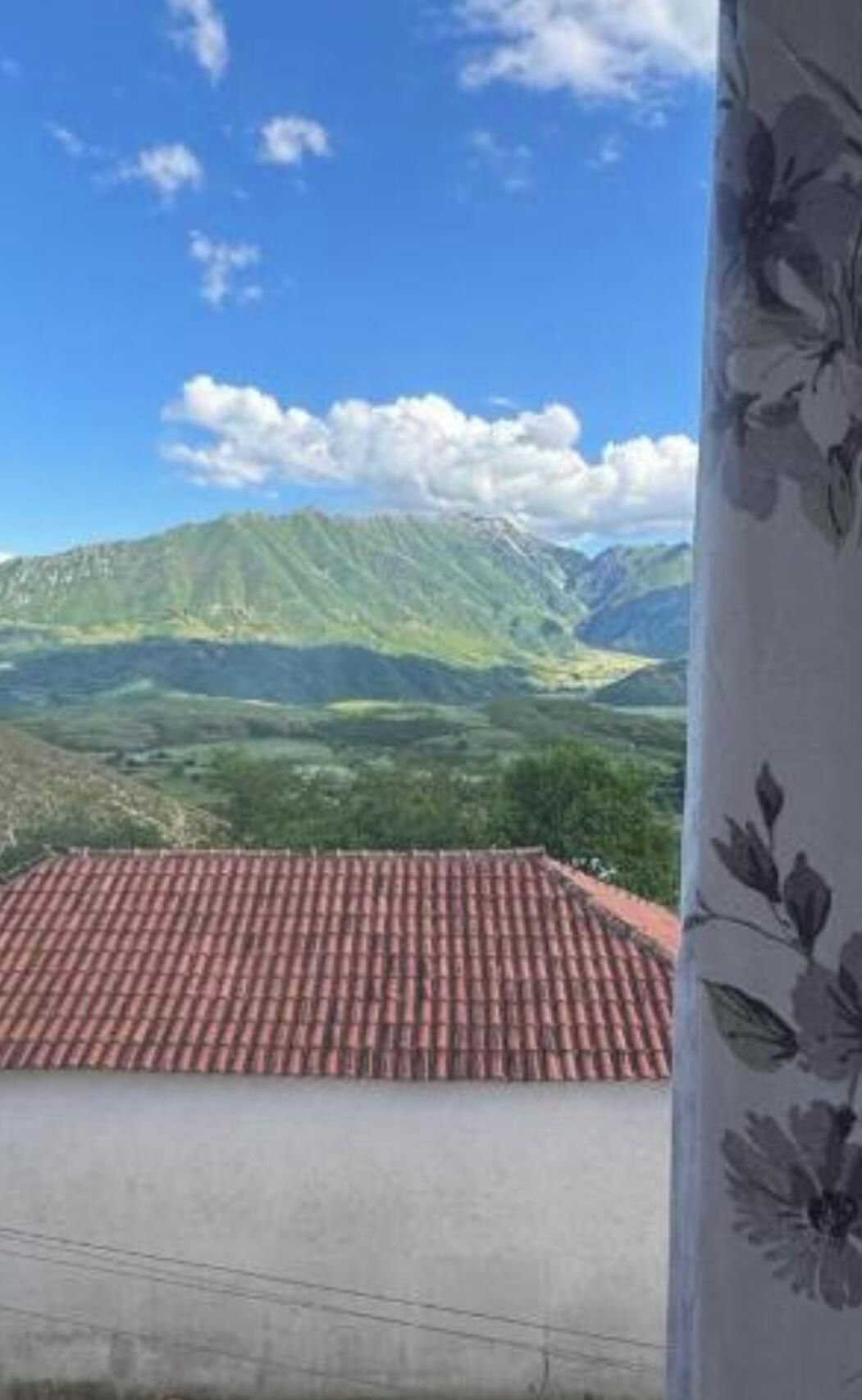 A view of a mountainous landscape with a red-tiled roof and a white wall.