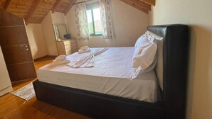 A bedroom with a wooden ceiling, a bed with white linens, a dark headboard, a dresser, and a window with curtains.