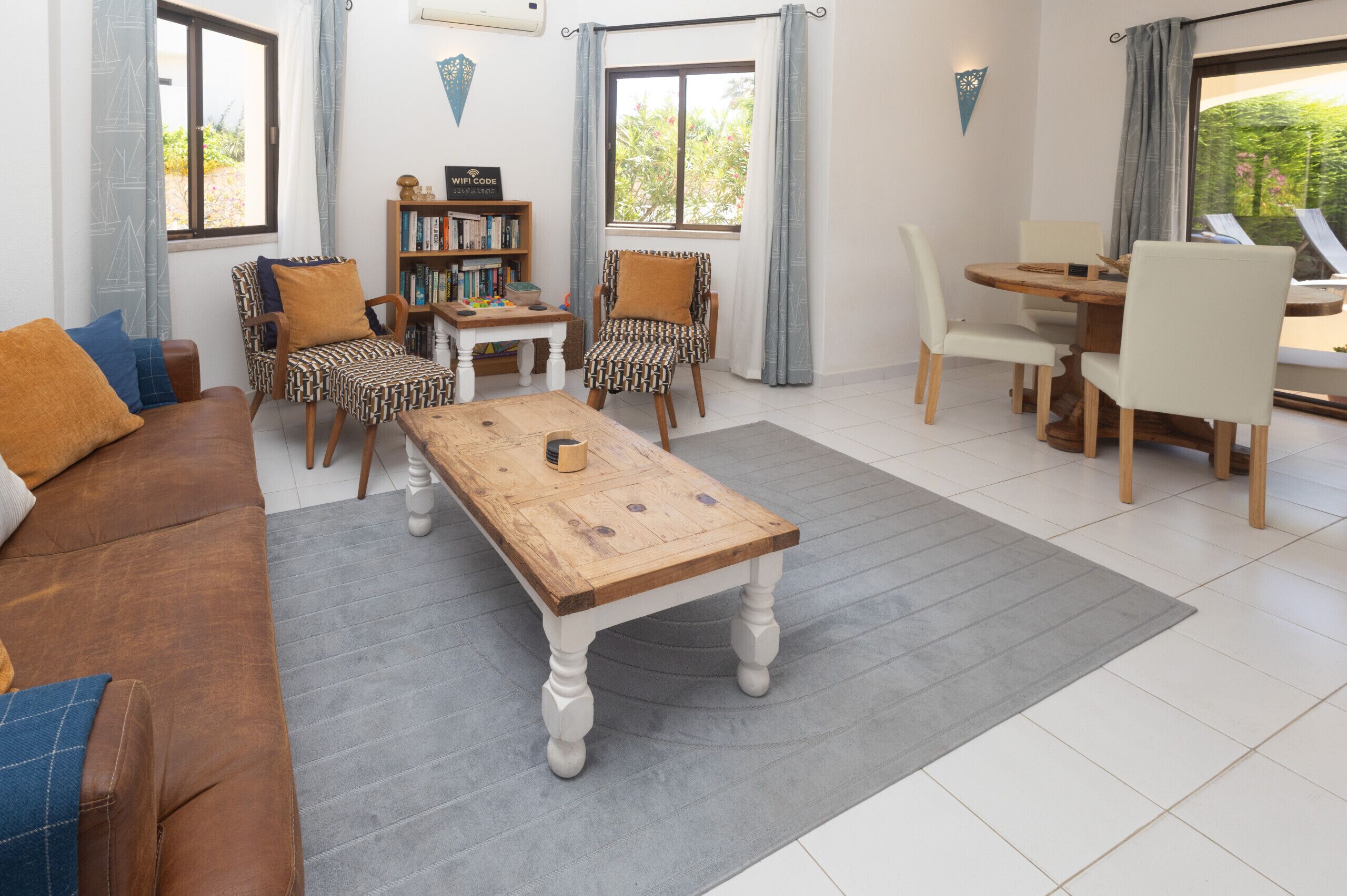 A living room with a sofa, two patterned chairs, a wooden coffee table, a bookshelf, and a dining area with a table and chairs.