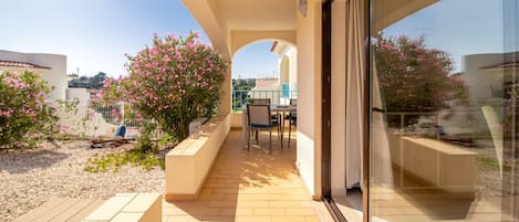 Un balcon donnant sur un jardin, une table avec des chaises et une porte vitrée menant à un espace intérieur.