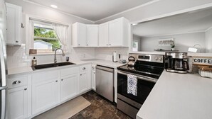 A modern kitchen with white cabinetry, a built-in oven, a coffee maker, and a window with curtains.