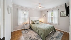 A bedroom with a bed, nightstands, a ceiling fan, and two windows with curtains.