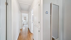 A hallway with white walls, wooden flooring, and a door with a thermostat.