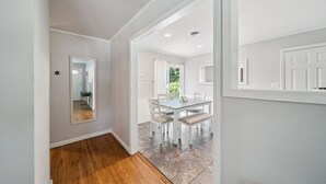 A hallway with a wooden floor leading to a dining area with a table and chairs.