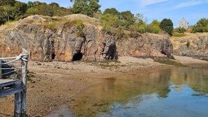 A rocky shoreline with clear water, a wooden dock, and a stone building in the background. - Waterfront Retreat with Loft & Harbor Views in Historic Eastport, Maine (Eastport)