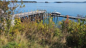 A wooden dock extending into a calm body of water, surrounded by lush greenery and distant landforms. - Waterfront Retreat with Loft & Harbor Views in Historic Eastport, Maine (Eastport)