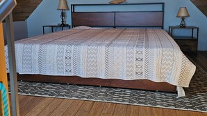 A bedroom with a sloped ceiling, a bed with a patterned bedspread, two bedside tables with lamps, and a decorative fish on the wall. - Waterfront Retreat with Loft & Harbor Views in Historic Eastport, Maine (Eastport)