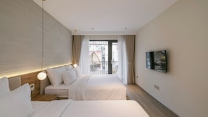 Habitació d'hotel moderna amb un llit gran, una taula de nit, un llum penjant, televisió muntada a la paret i vista al balcó exterior.