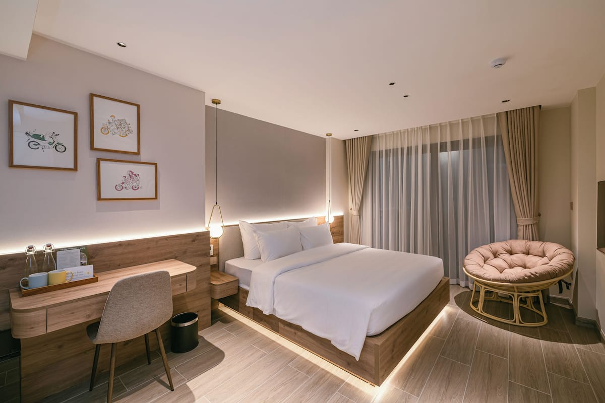 A modern hotel room with a bed, a desk, a chair, and a round seating area.
