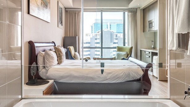 Una habitación de hotel moderna con una cama grande, un separador de vidrio, vistas a la ciudad y un baño con bañera.