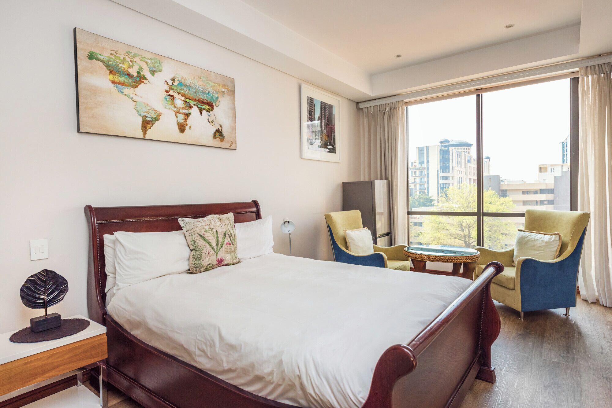 Een hotelkamer met een groot bed, twee fauteuils, een kleine tafel en een wereldkaartschilderij.